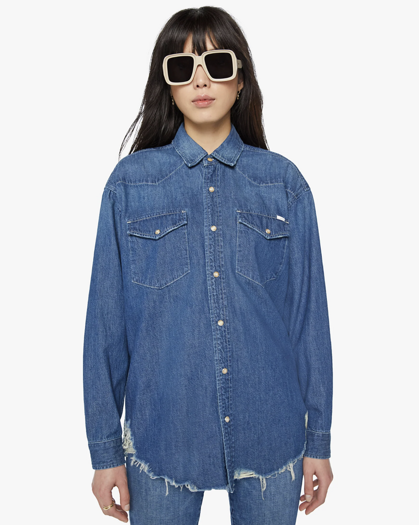 An oversized Western-inspired denim button-up with front patch pockets and a raw, curved hem. Made from 100% cotton, Dopenhagen is a vintage-blue wash with subtle fading throughout. By Mother Denim, now available at After Eight. 