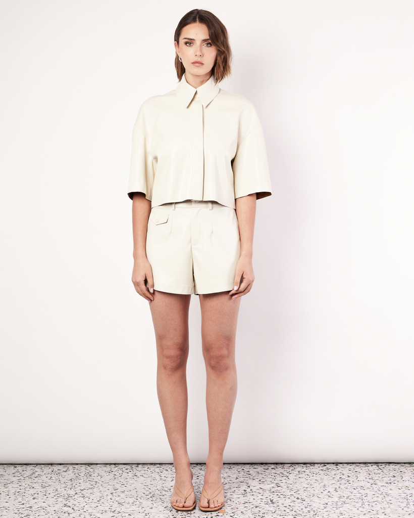 The Vegan Leather Cropped Shirt in cream is meticulously crafted from supple vegan leather, offering a luxurious feel against your skin. It's expertly tailored for an oversized silhouette, ensuring both comfort and style. Style with the coordinating Vegan Leather Shorts. By Romy, now available at After Eight. 