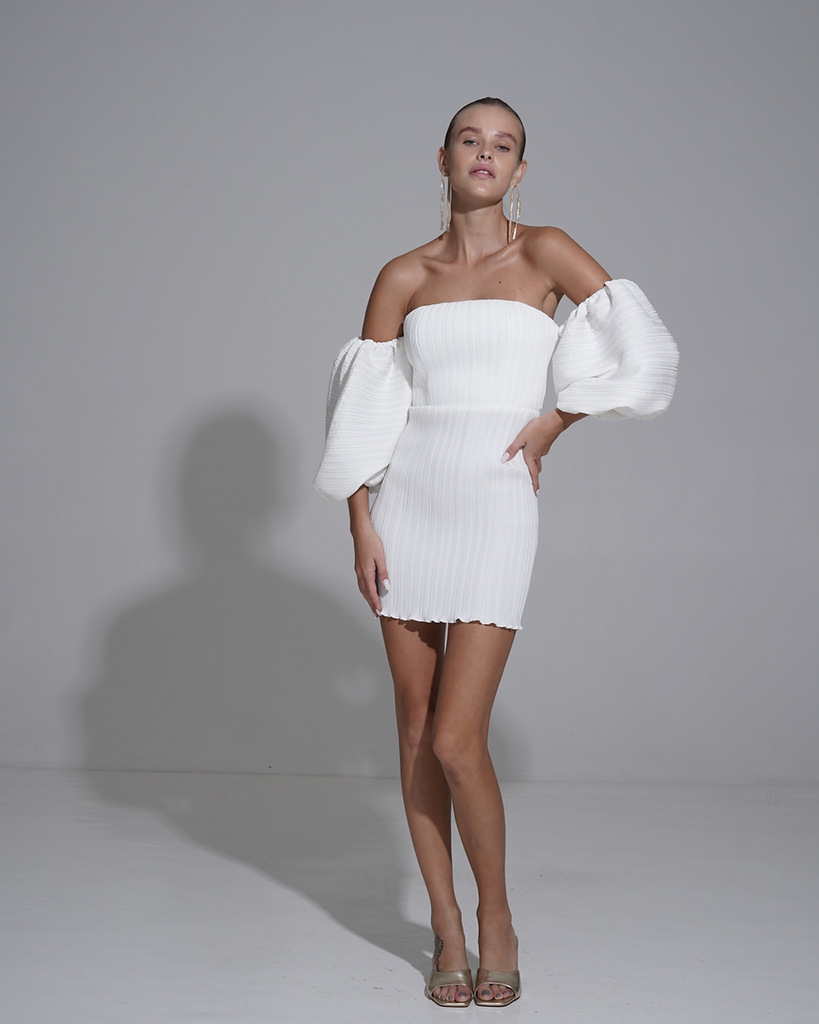 The Sirene Mini is an chic expression of contemporary and classic glamour.  This strapless number emphasises the perfect amount of décolletage whilst the bell sleeve incorporates a chic and refined element. The highly engineered ribbed pleats embrace the female form through torso before finishing with a gently fluted hem. In combination with it's extravagant sleeves the gown offers a feminine and flattering silhouette that embodies old Hollywood glamour. By L'IDEE WOMAN, now available at After Eight. 