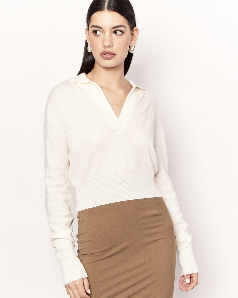 The Cropped Collared Sweater is a trans-seasonal knitwear essential, featuring a collar, deep-v neckline, and cropped hem. It is crafted from a luxurious Wool Cashmere blend in Cream. By Romy, now available at After Eight. 