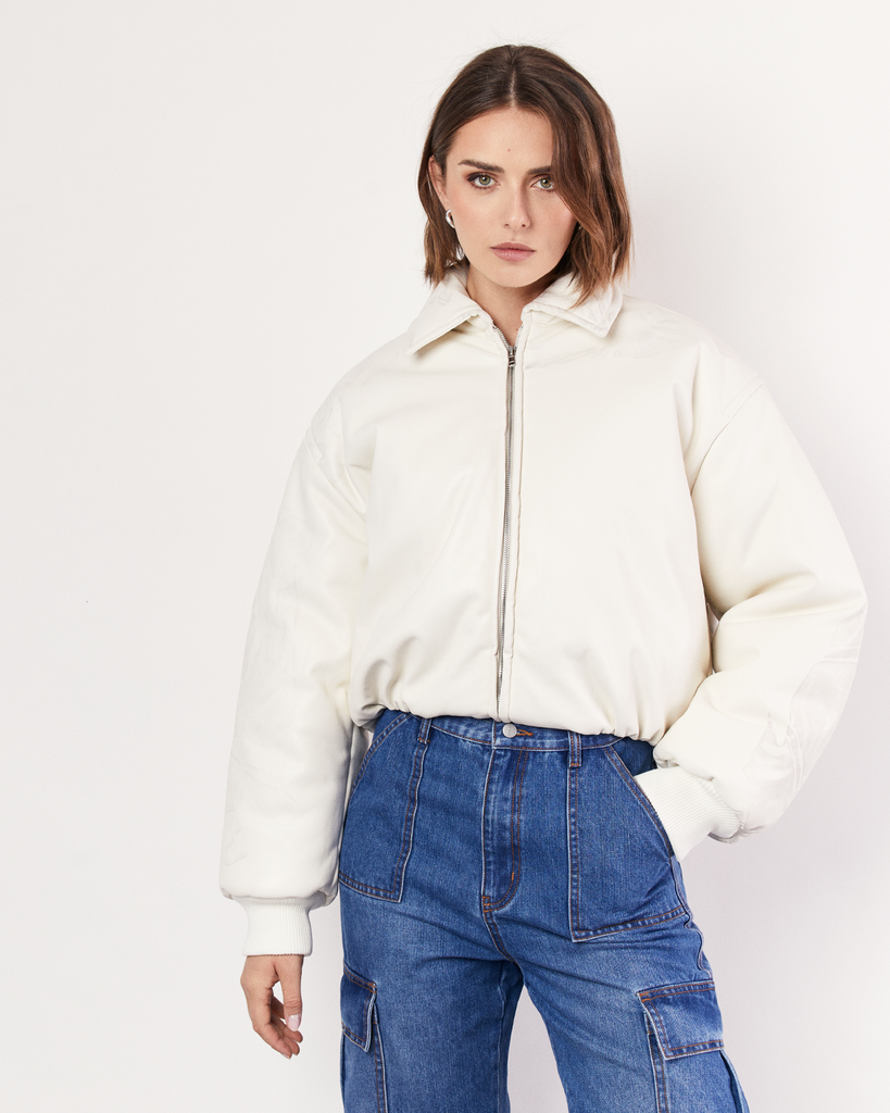 The Romy best-selling Padded Bomber Jacket is a must-have in your winter wardrobe, featuring a collar, gathered hem, and ribbed knit cuffs. It is crafted from a buttery soft Vegan Leather in Cream. By Romy, now available at After Eight. 