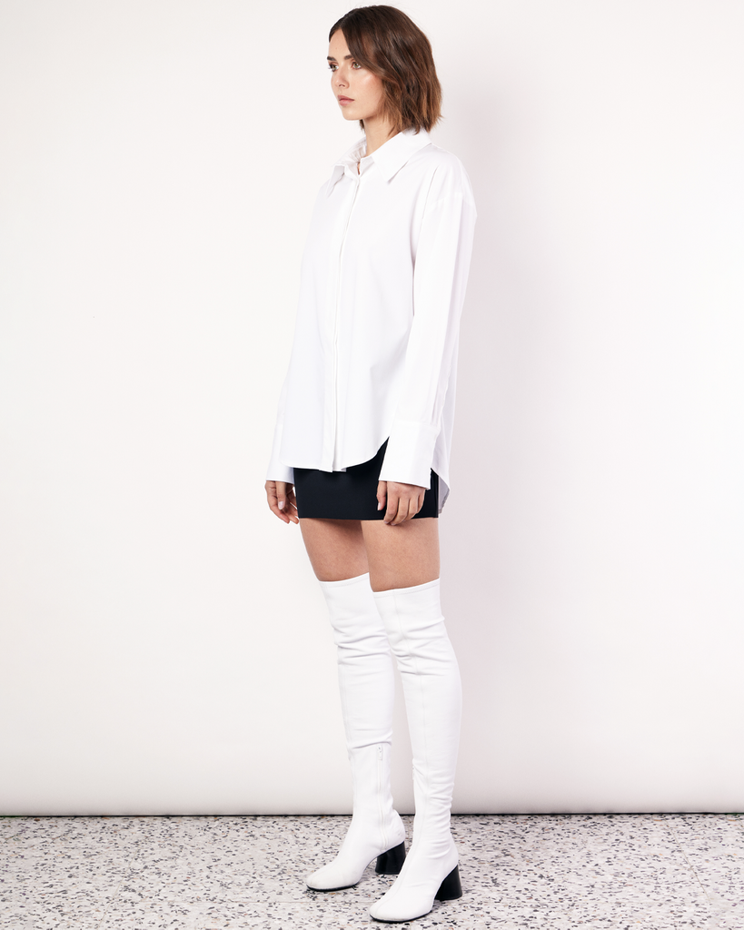The Classic Shirt in white is a wardrobe icon. Cut oversized with a scooped hem and elongated cuff, this shirt is the perfect pairing for achieving a timeless look. Crafted from a regenerated cotton blend with a touch of stretch, it's not only stylish but also less likely to crease compared to 100% cotton, ensuring you stay effortlessly chic all day long. By Romy, now available at After Eight. 