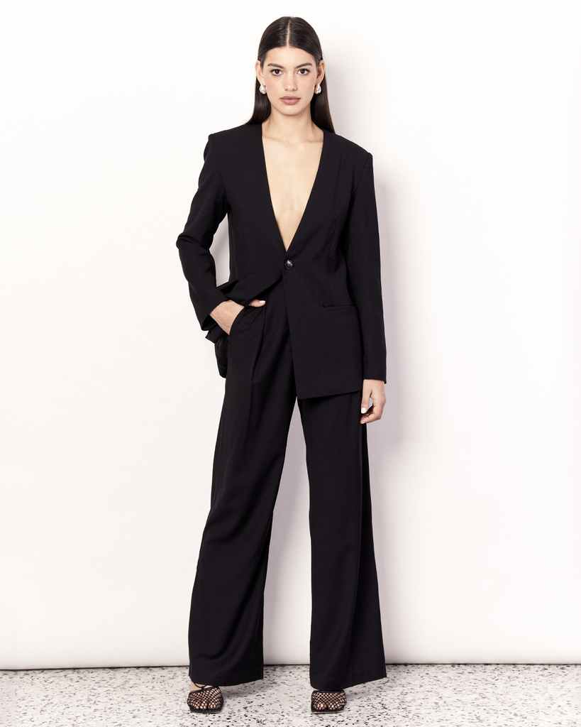 The Collarless Blazer is a versatile tailored silhouette featuring two front pockets, a button closure and a collarless neckline. It is fully lined and is crafted from a soft wool blend in Black. By Romy, now available at After Eight. 
