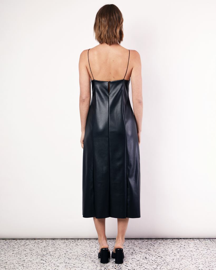 The Deep V Vegan Leather Midi Dress is a chic style featuring flattering front seam detailing and rouleau straps. It is crafted from a buttery soft Vegan leather fabrication in Black. By Romy, now available at After Eight. 