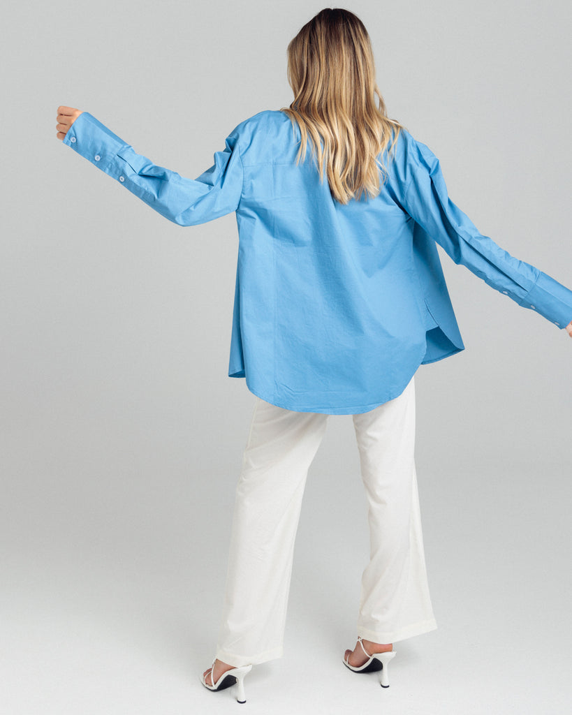 The Cotton Shirt in blue has elongated cuffs and a scooped hemline. By Romy, now available at After Eight. 